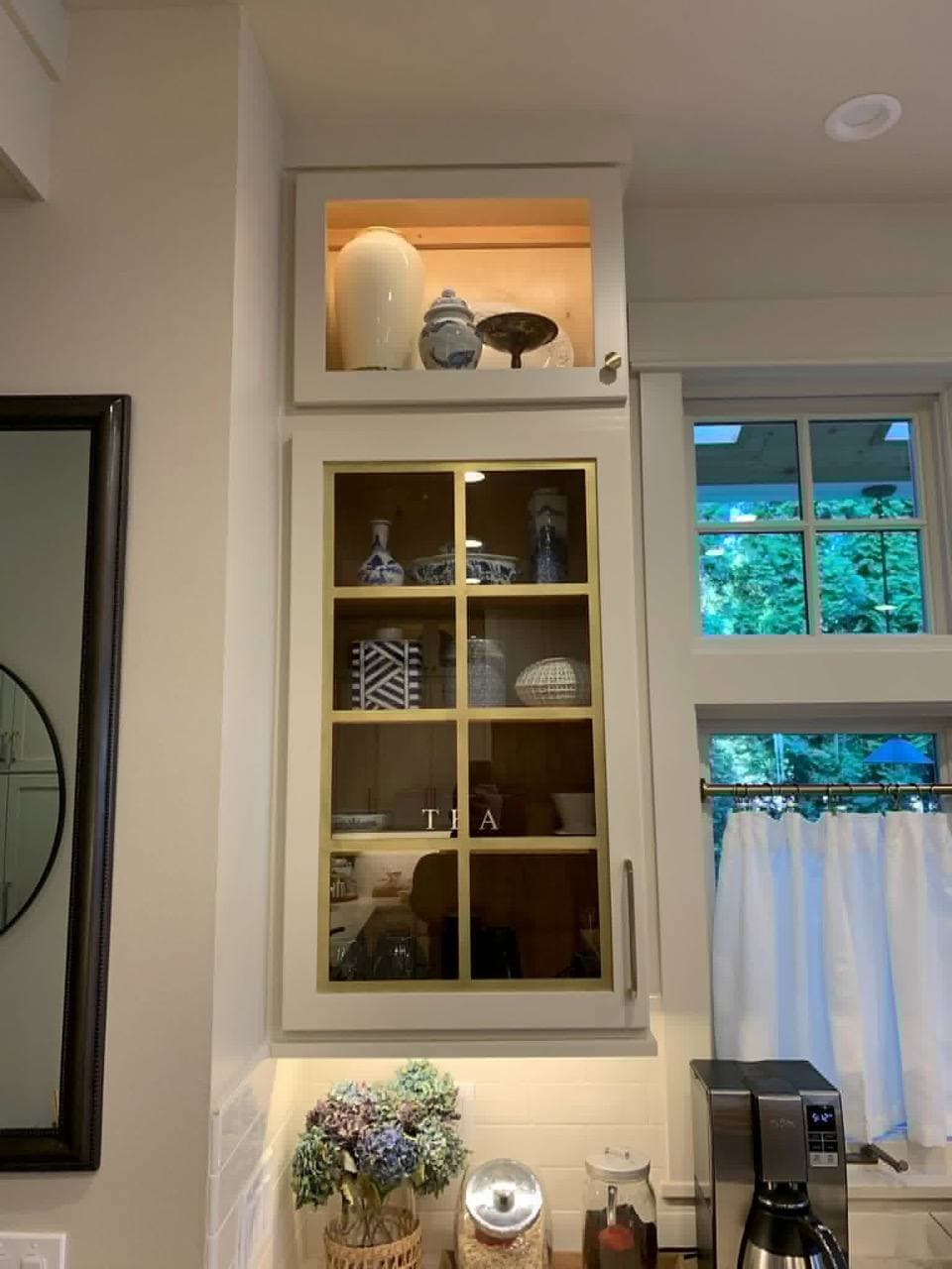 Glass-front display cabinet with bronze muntin bars dividing the panes, filled with dishware.
