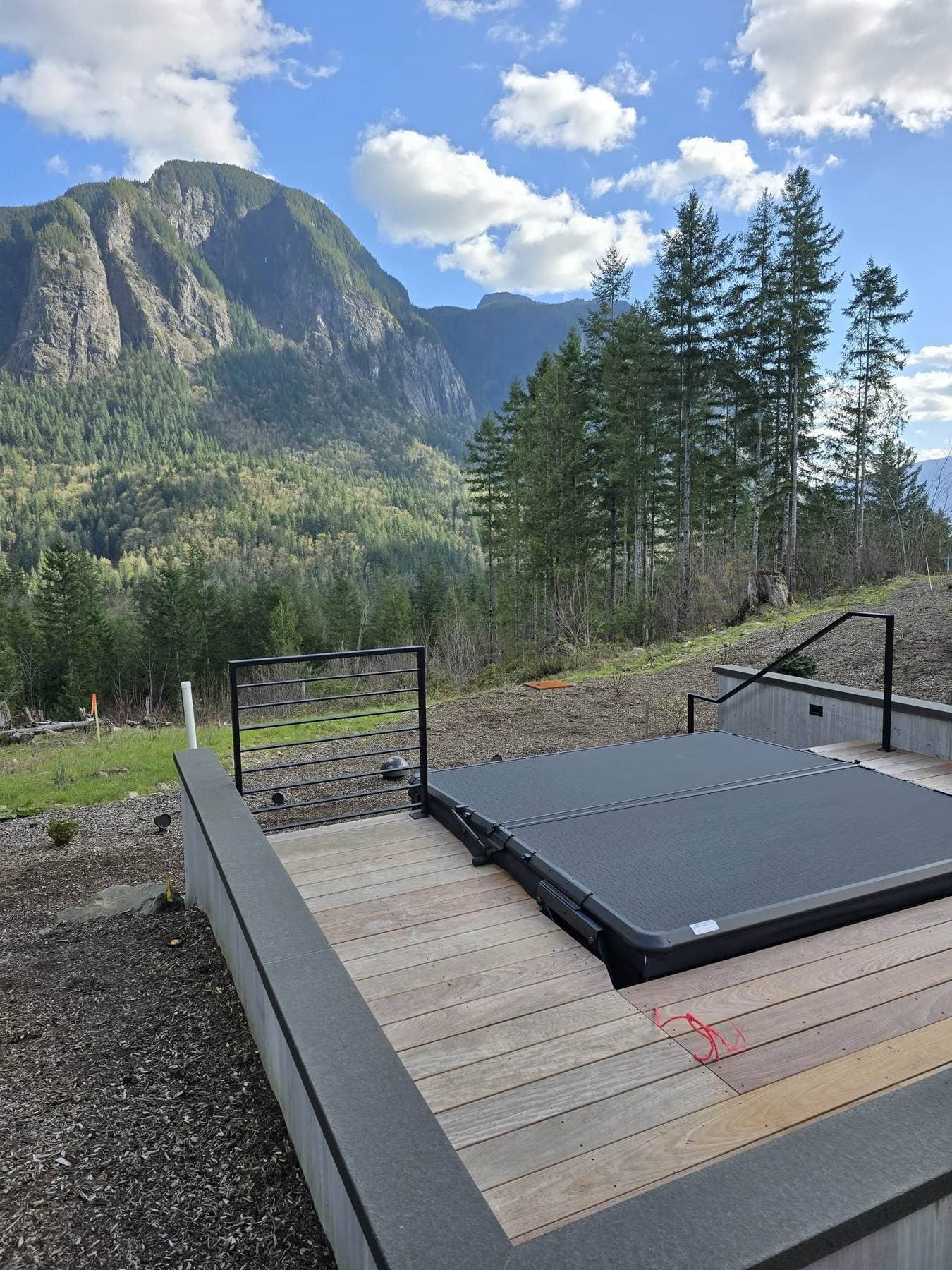 Steel bar-rail deck gate on a concrete-and-wood deck overlooking a forested mountain valley.