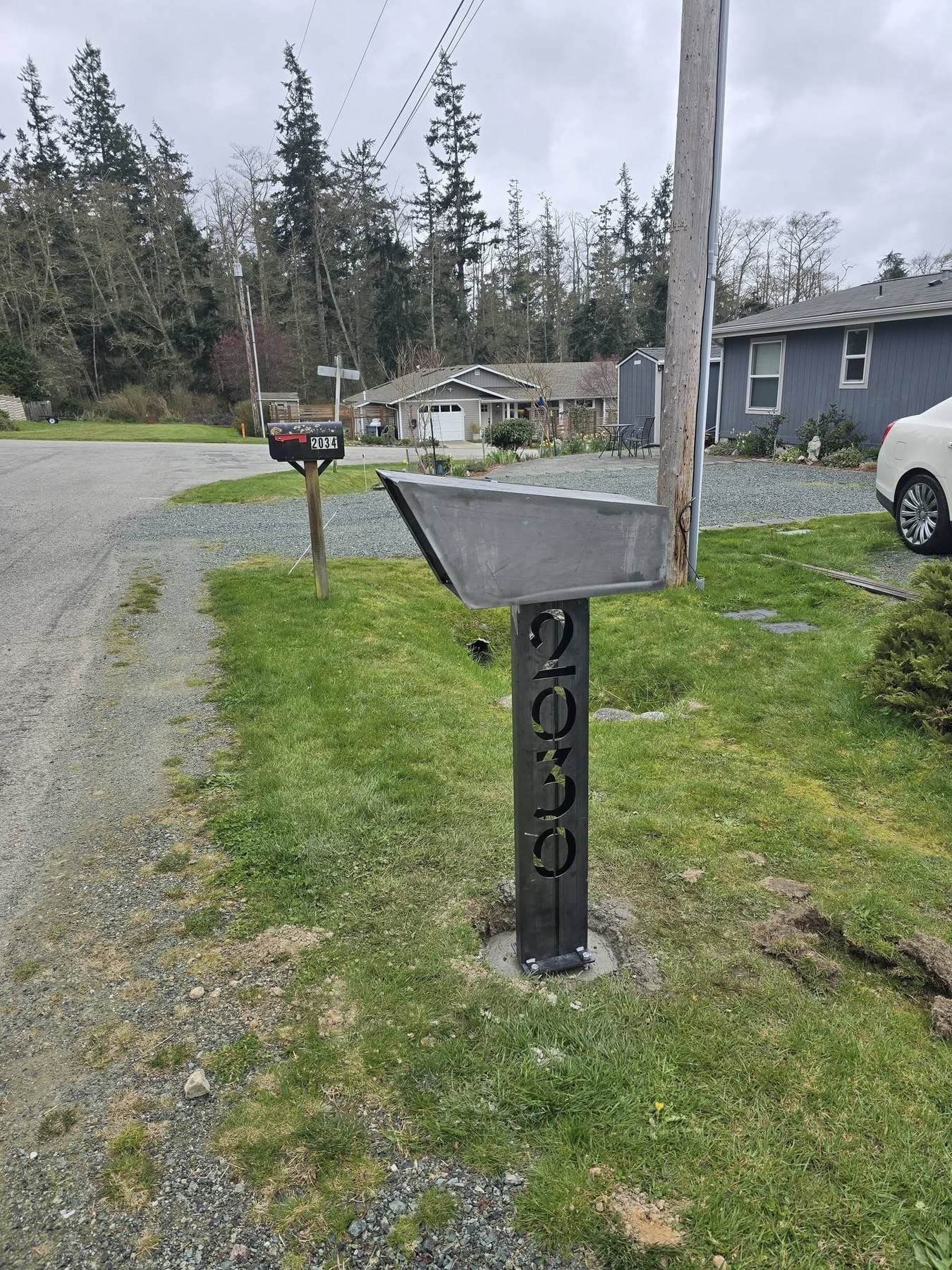 Custom steel mailbox with an angular hooded top and house numbers cut through the steel post, set at the curb.