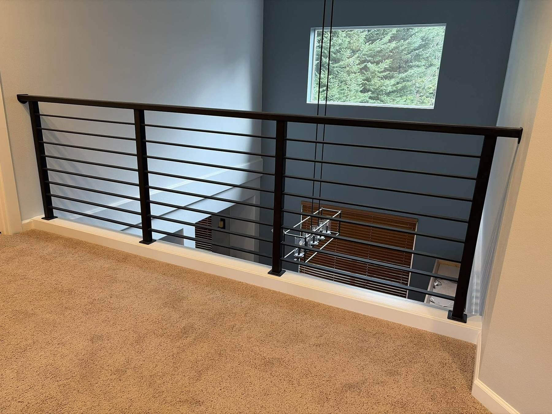 Blackened steel horizontal-bar railing wrapping a loft landing, with a window and staircase in the background.
