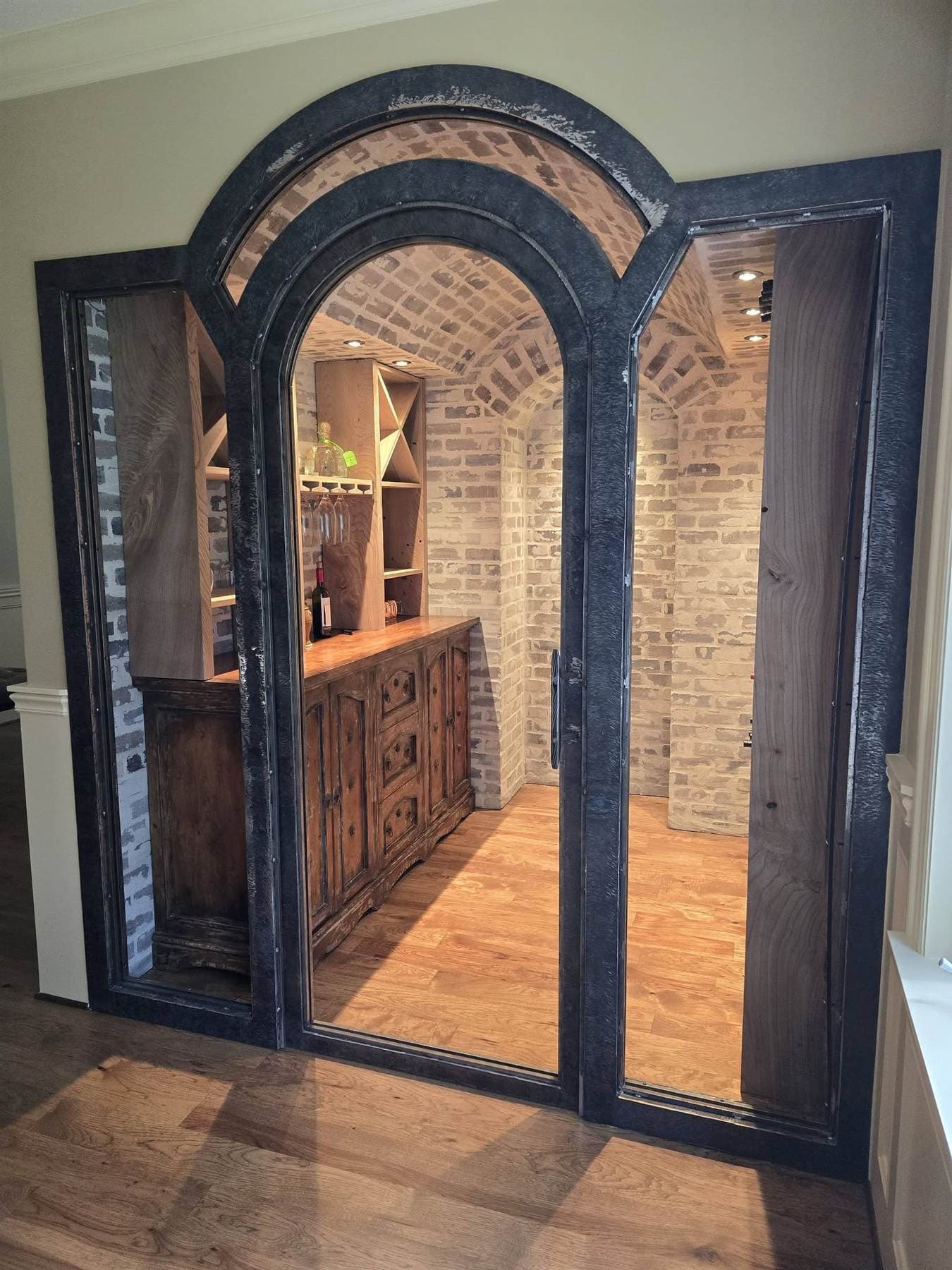 Arched steel-and-glass double door opening into a brick barrel-vaulted wine cellar with wood wine racks.