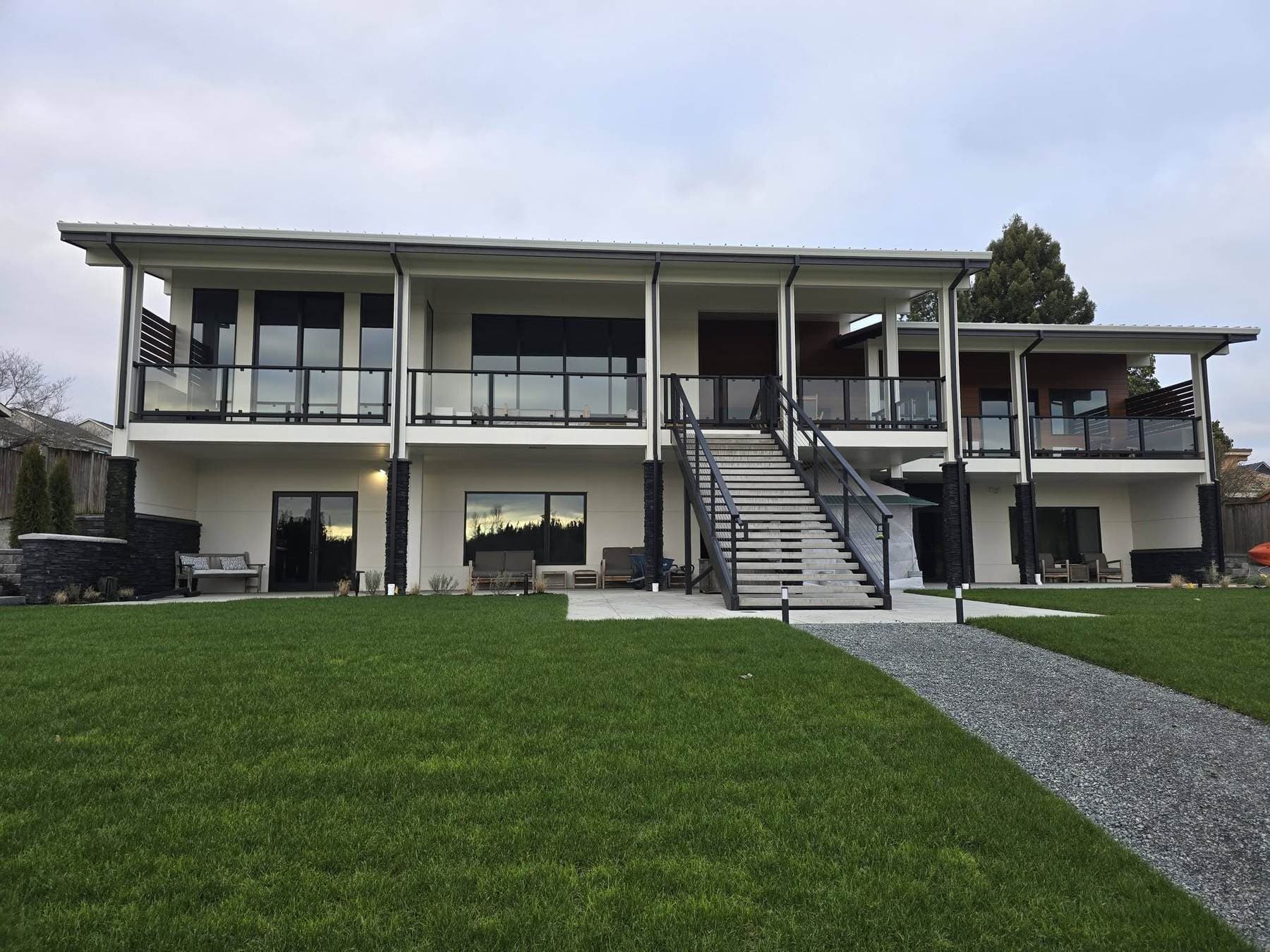 Two-story modern home with matching black-framed glass balcony railings and a long exterior stair with cable railing, custom-built by JWALL Fabrication.